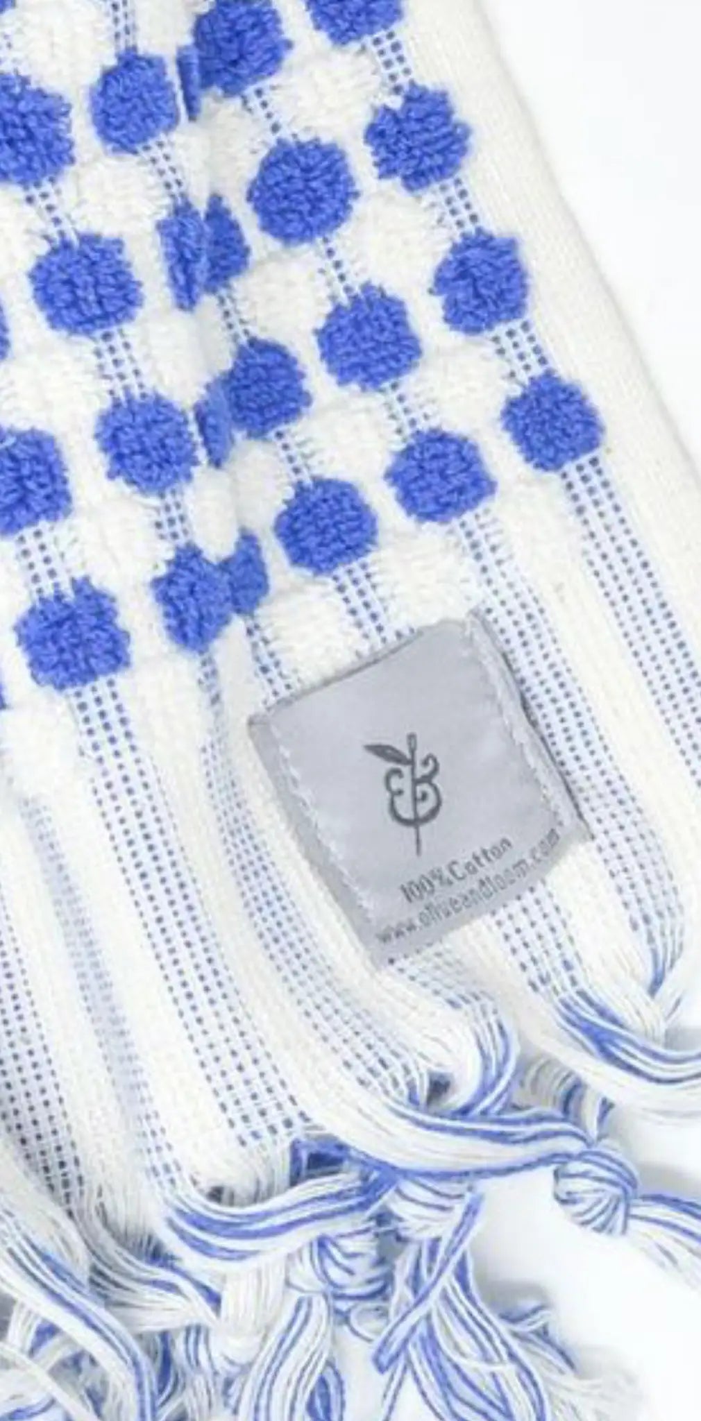 "White cotton label with blue polka dots and fringed edges, featuring a gray stitched label at the bottom."