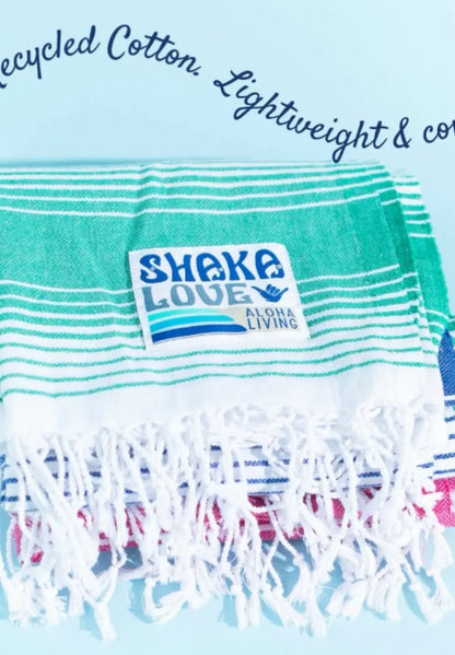 "Stack of lightweight recycled cotton towels in green and blue stripes with white fringe, featuring a 'Shake Love' label."