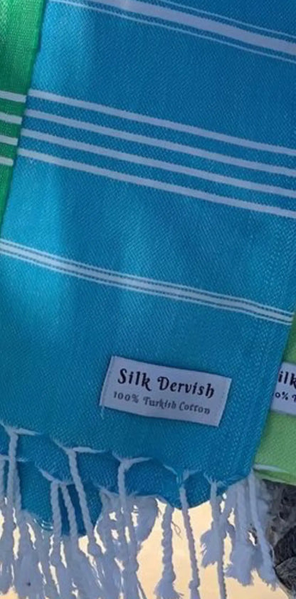 "Turquoise cotton label with white stripes, featuring 'Silk Dervish' and '100% Turkish Cotton' text, fringed edges."
