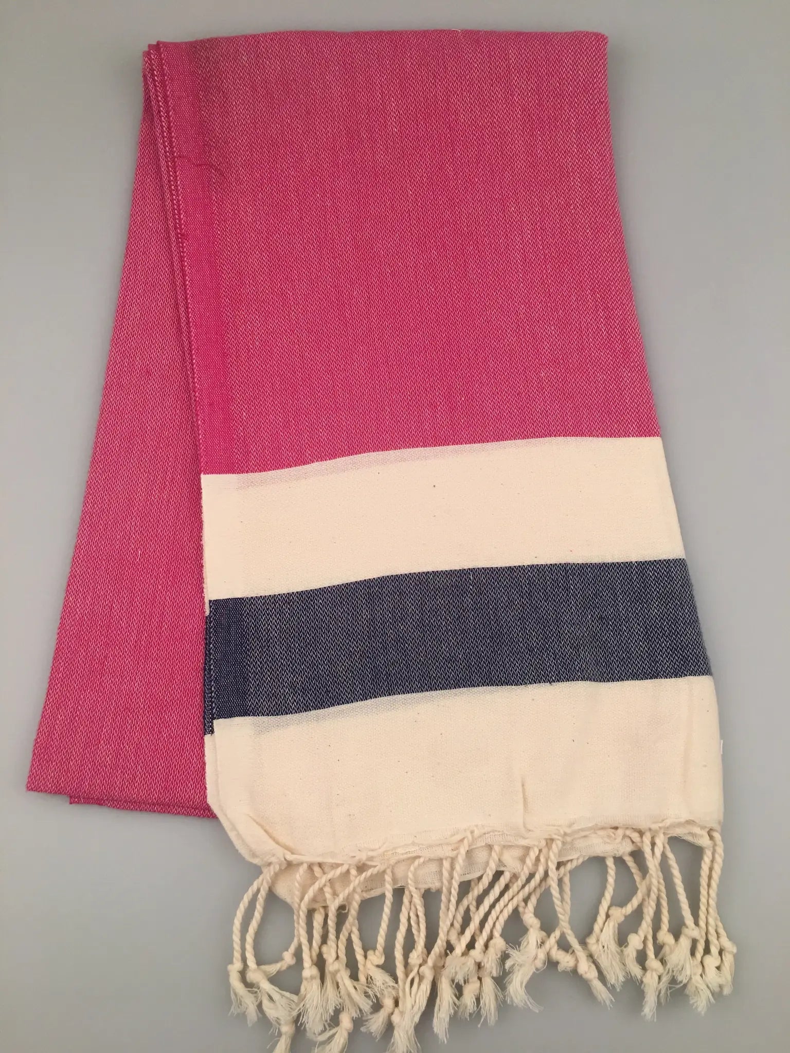 "Blaundos Turkish towel peshtemal in pink with a cream and navy striped border, featuring fringed edges."