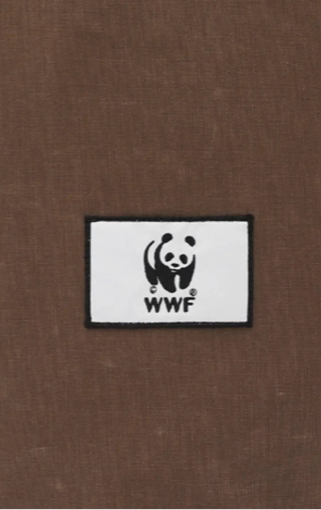 White rectangular cotton label with black border, featuring a panda graphic and "WWF" text, on a brown fabric background.