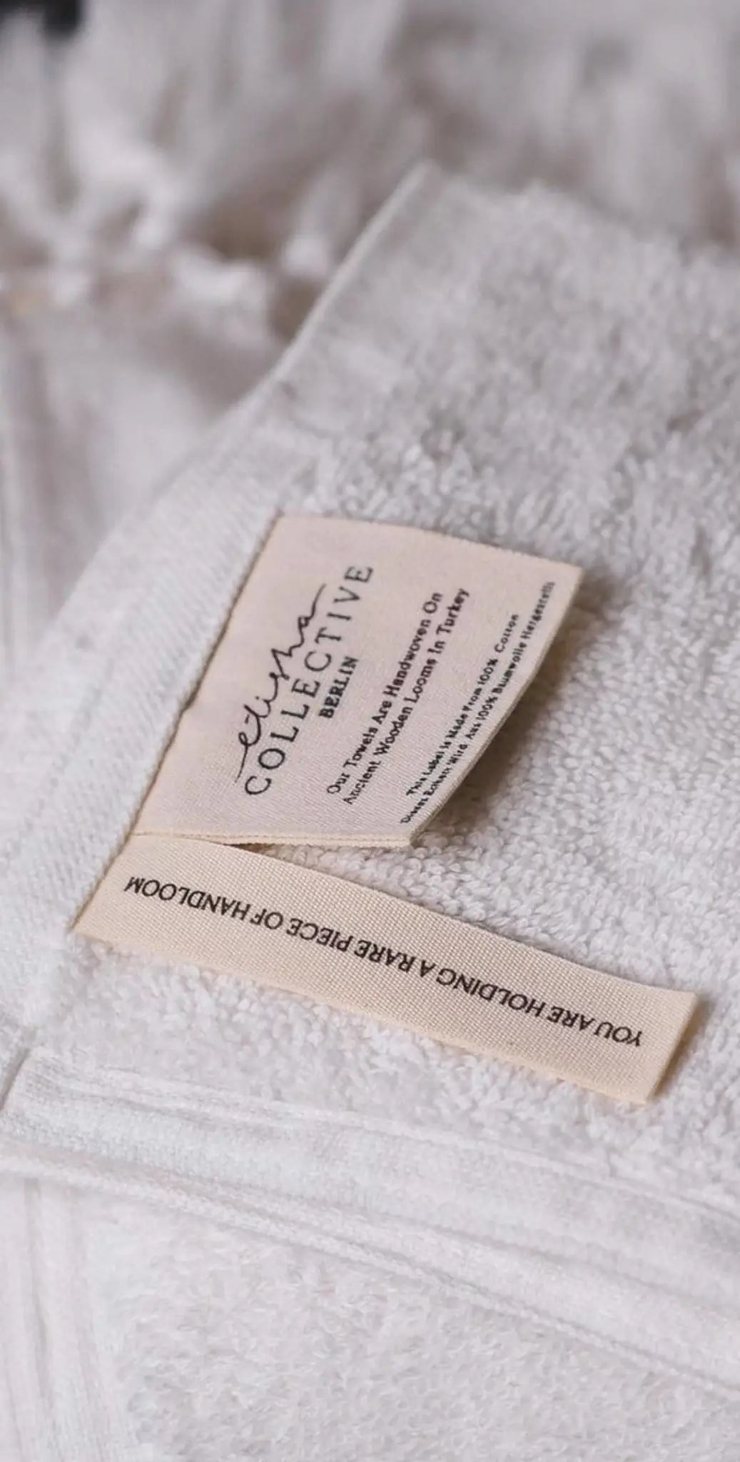 "White cotton label with black text, featuring care instructions and branding, attached to textured fabric."