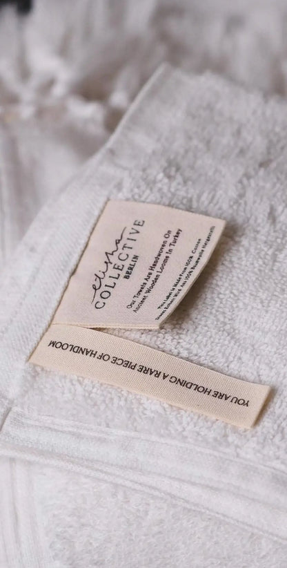 "White cotton label with black text, featuring care instructions and branding, attached to textured fabric."
