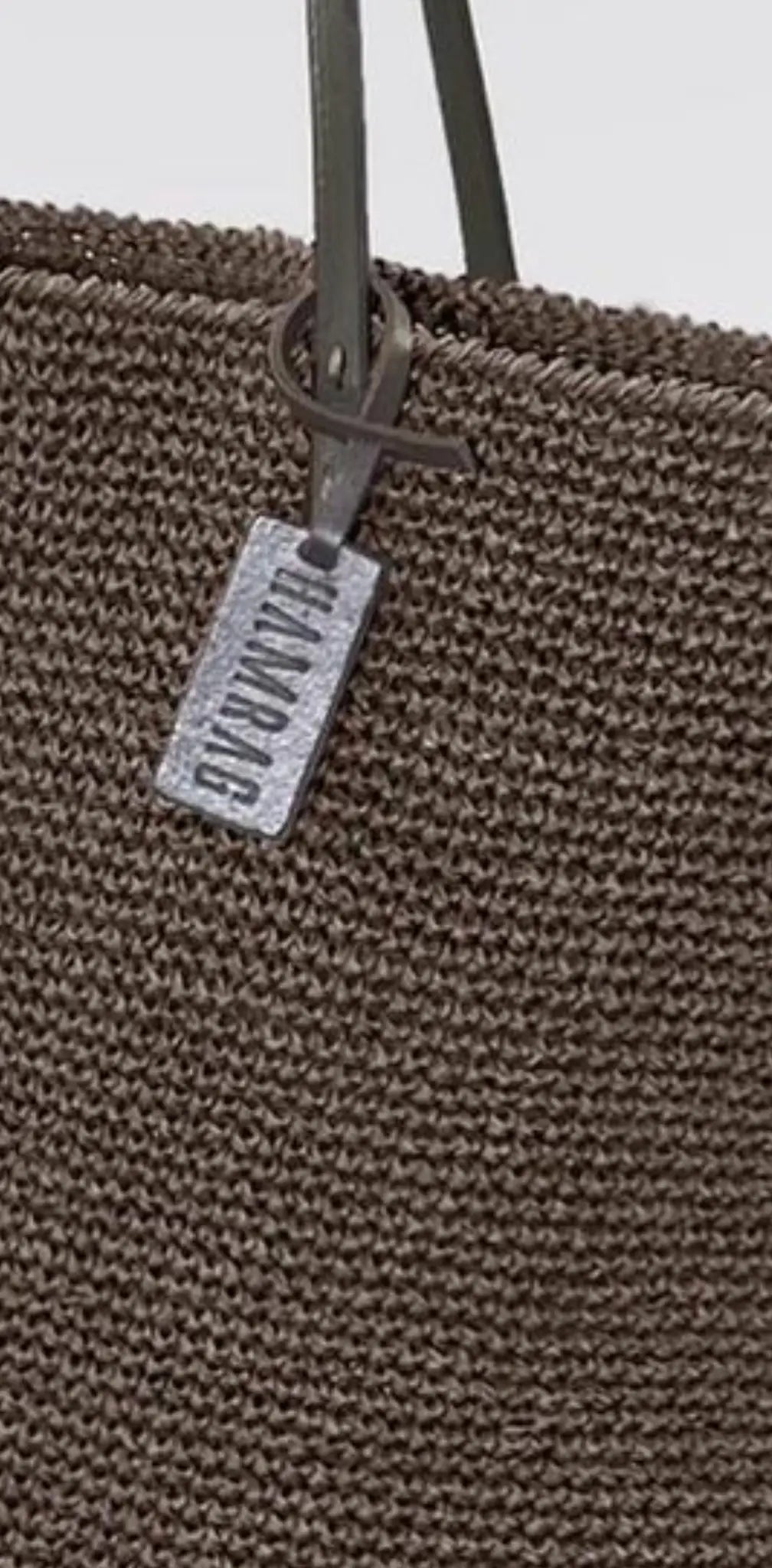 "Brown woven tote bag with long green handles and a rectangular silver label attached."