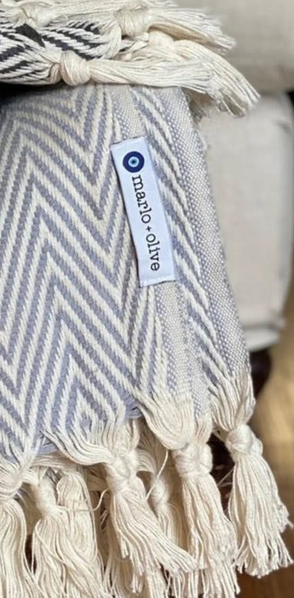 Cotton label with custom design, featuring a blue circle logo and text, attached to a woven blanket with cream and gray chevr