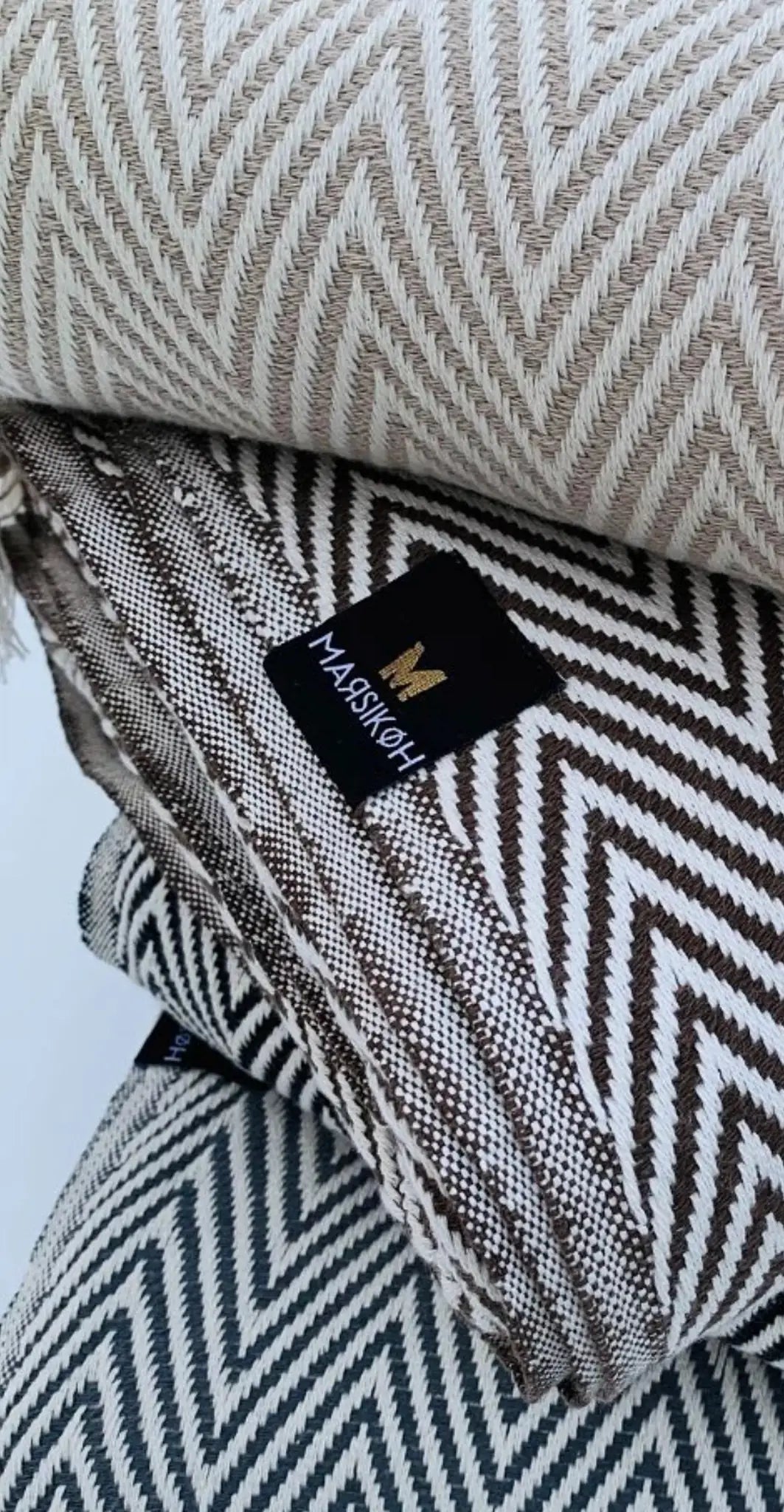 "Stack of cotton labels in beige and brown herringbone patterns, with a black logo tag on top."