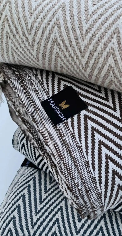 "Stack of cotton labels in beige and brown herringbone patterns, with a black logo tag on top."