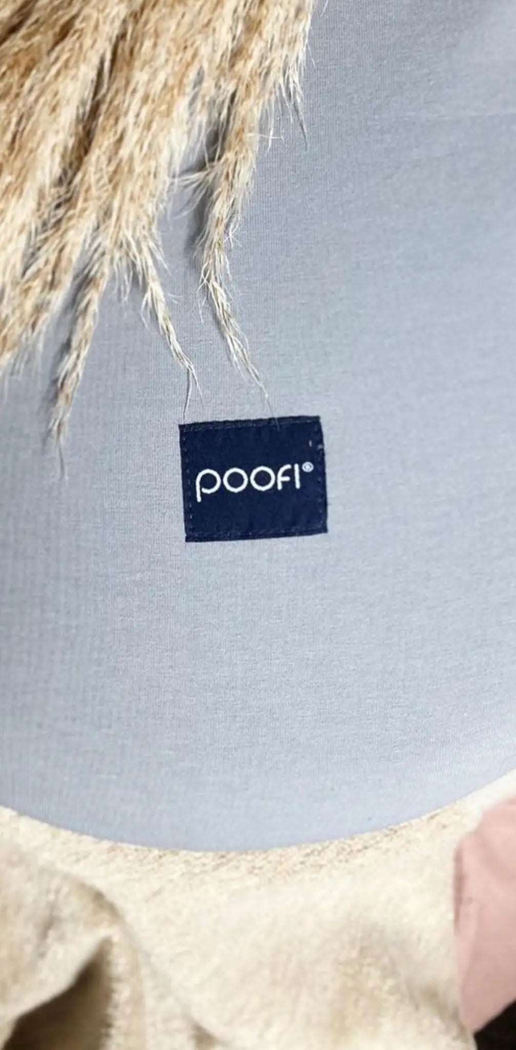 "Square navy label with white text 'poofi' on a gray fabric background with light tan furry texture."
