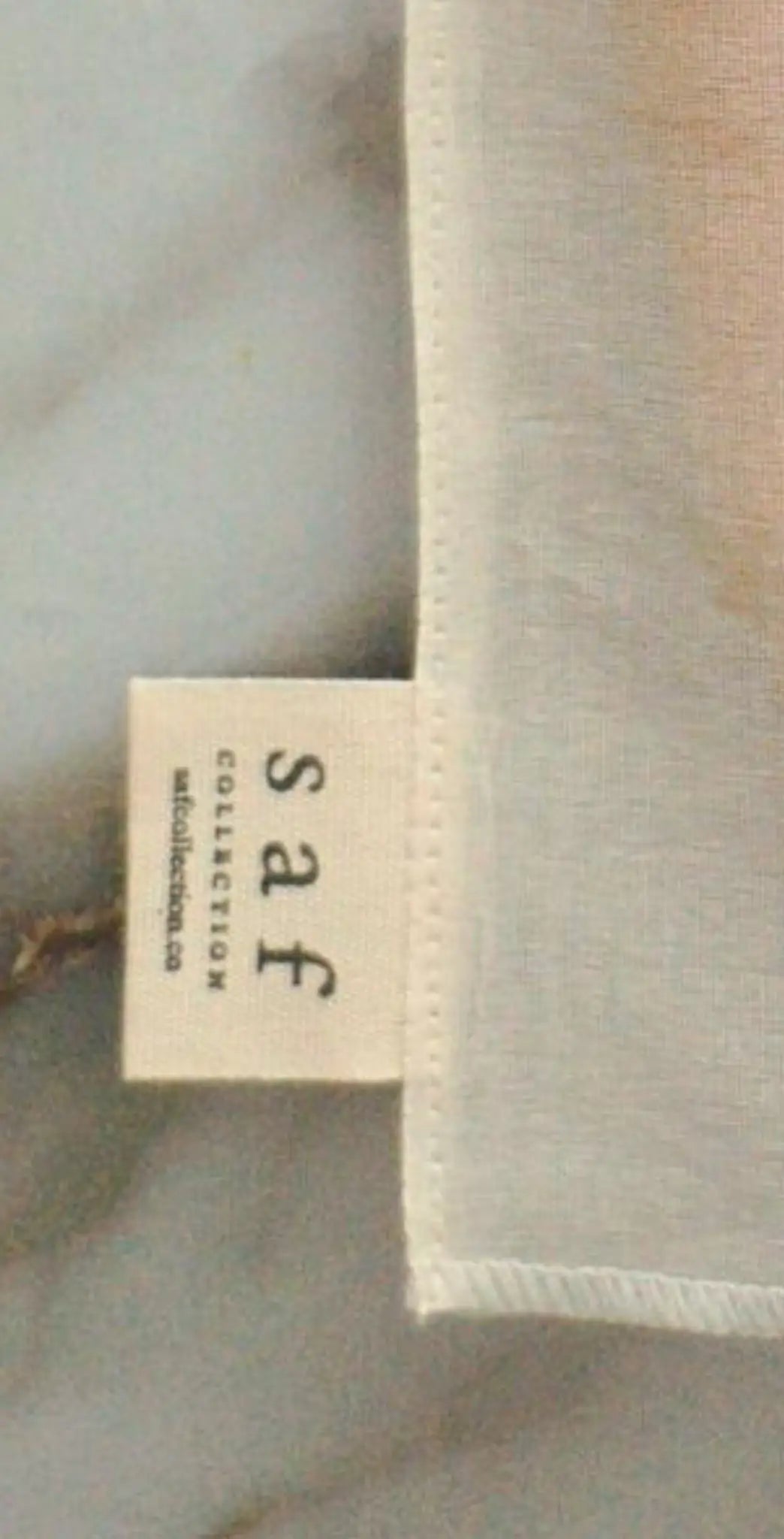 "Small fabric label with 'Saf' in lowercase letters, cream background, stitched edge, resting on a marble surface."
