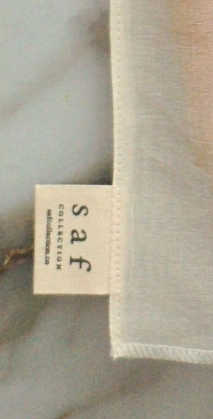 "Small fabric label with 'Saf' in lowercase letters, cream background, stitched edge, resting on a marble surface."