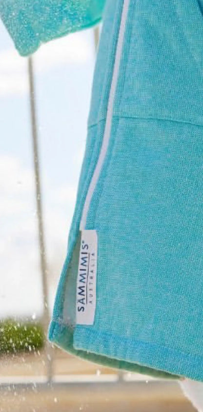 Light blue cotton label with white text reading "SAMMIMIS," attached to a turquoise garment, side view.